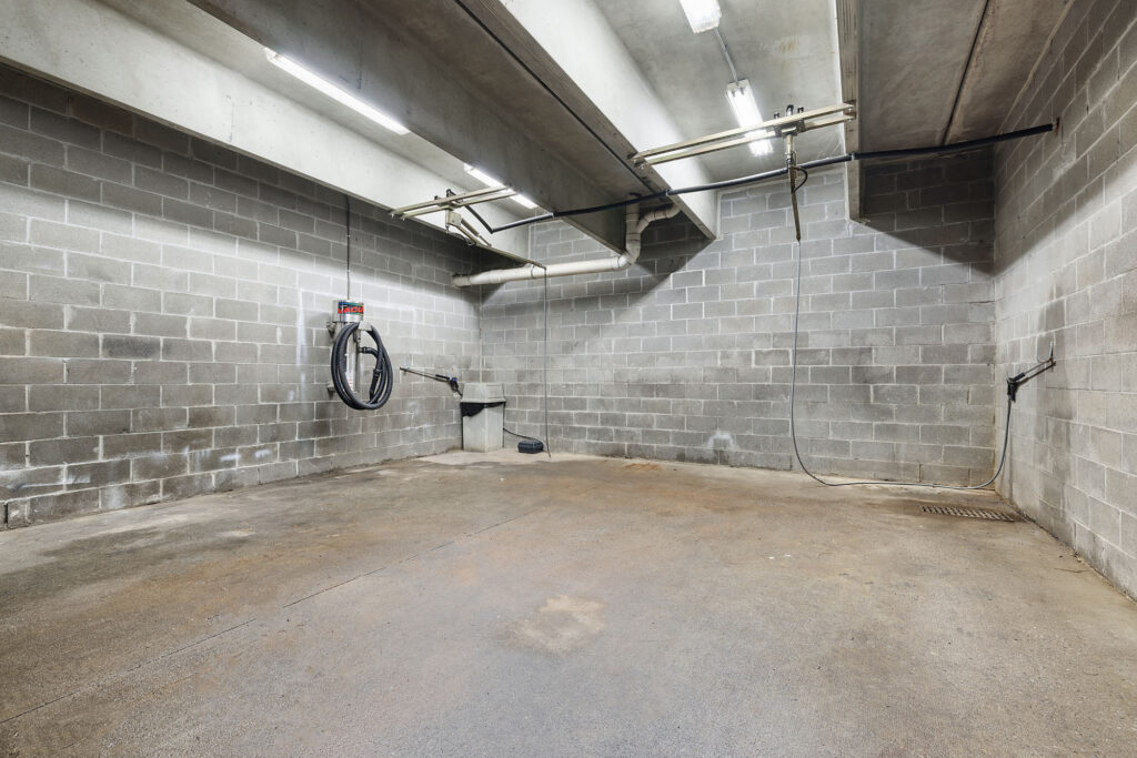 An empty concrete car wash bay with a wall-mounted vacuum and overhead plumbing.