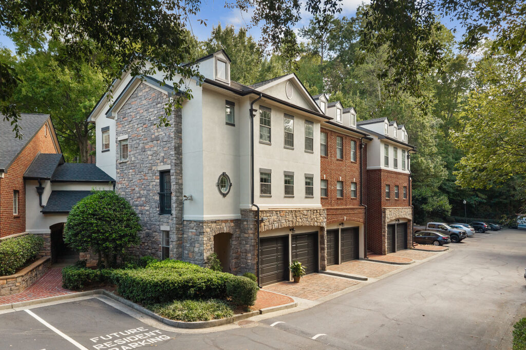 A multi-story residential building with stone and brick siding, featuring ground-level garages and a paved parking area.