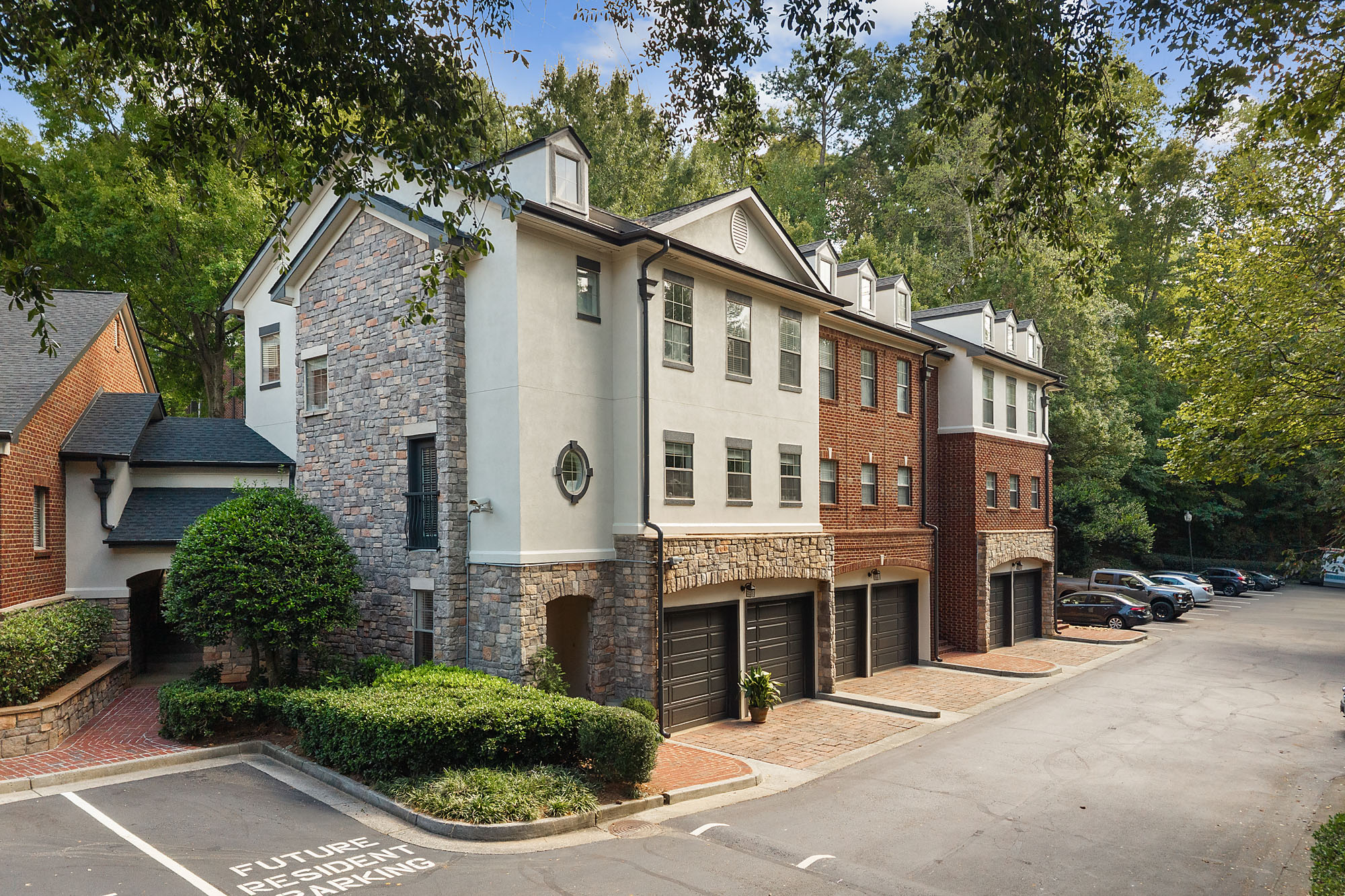 A multi-story residential building with stone and brick siding, featuring ground-level garages and a paved parking area.