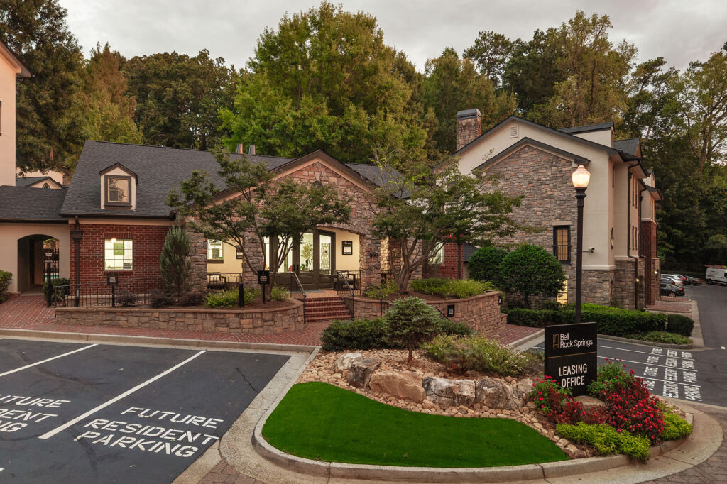 Bell Rock Springs apartment leasing office building with a stone and brick exterior, surrounded by trees and landscaping, with a sign indicating the leasing office and visitor parking.
