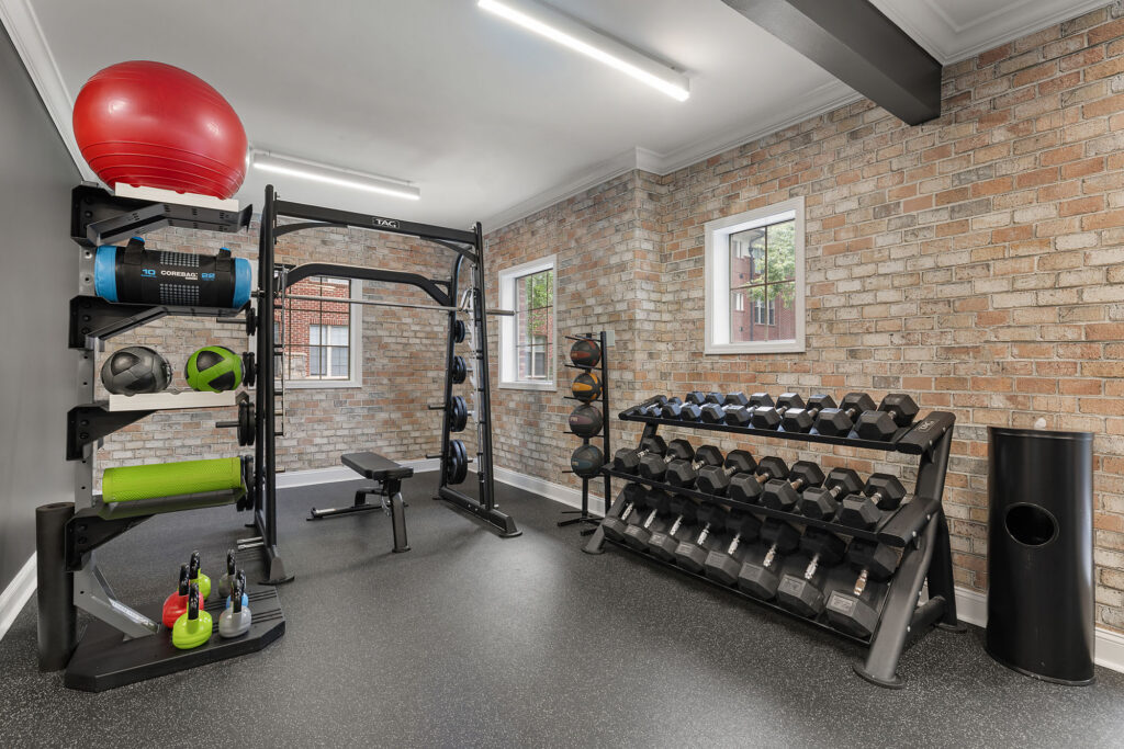 Home gym with a squat rack, adjustable bench, dumbbell rack, and a storage tower holding a red exercise ball, foam roller, and kettlebells.