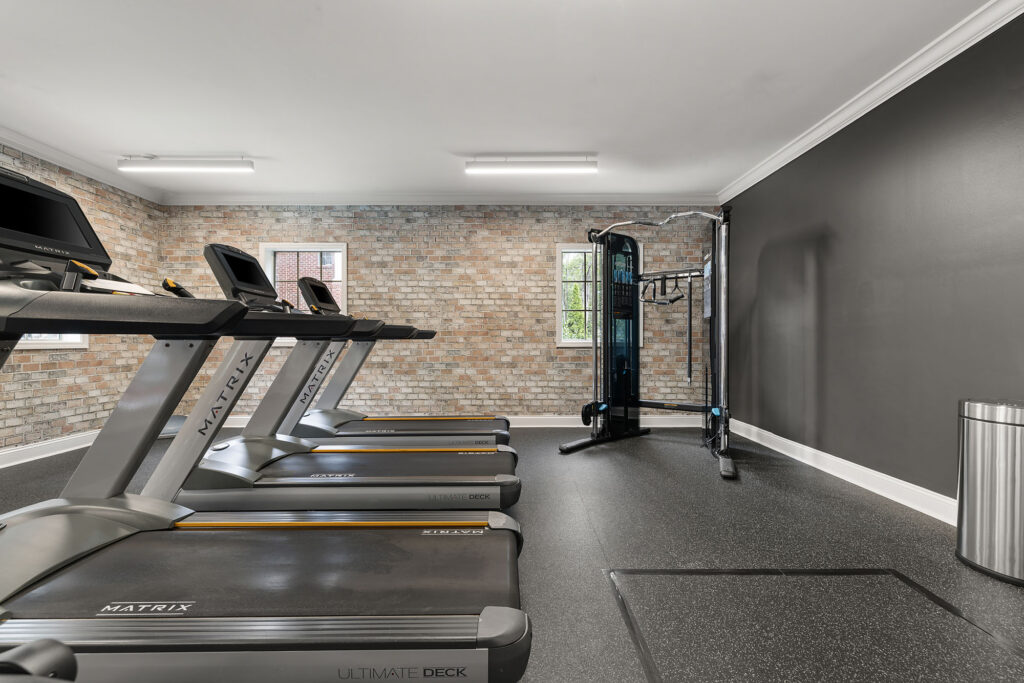 A fitness room with a row of three treadmills facing a brick wall and a multi-station weight machine.