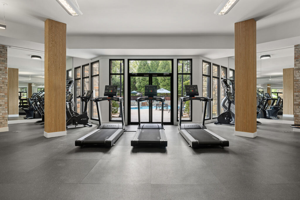 Three treadmills lined up in a gym, facing floor-to-ceiling windows that look out onto an outdoor swimming pool.