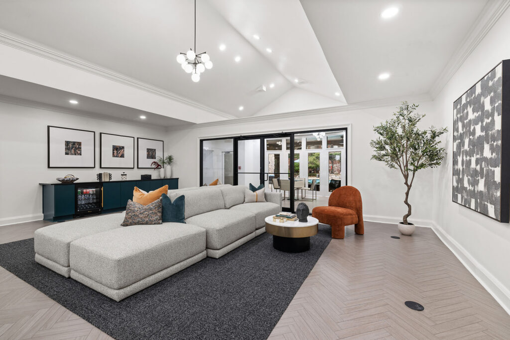 A bright living room featuring a large gray sectional sofa, a rust-colored accent chair, a round coffee table, and a dark blue console table, with sliding glass doors leading to a patio.