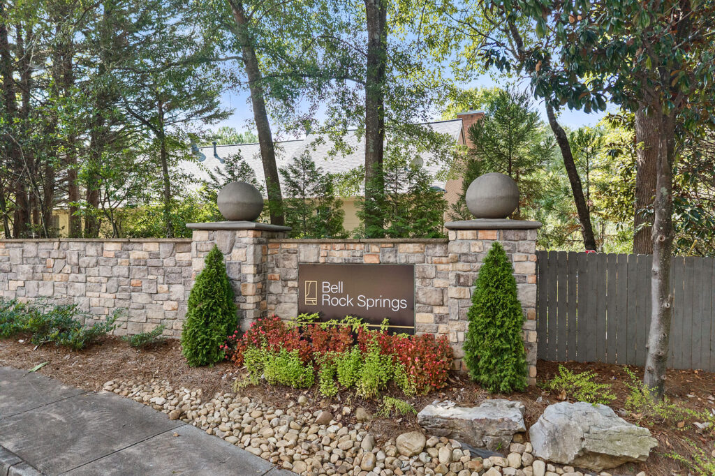 A stone wall with a sign reading Bell Rock Springs in front of a house obscured by trees.