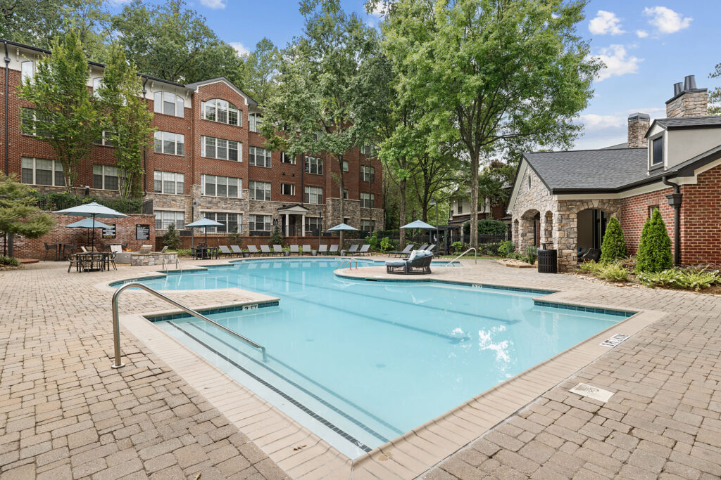 A swimming pool with lounge chairs and umbrellas on a brick patio in front of a multi-story brick apartment building.