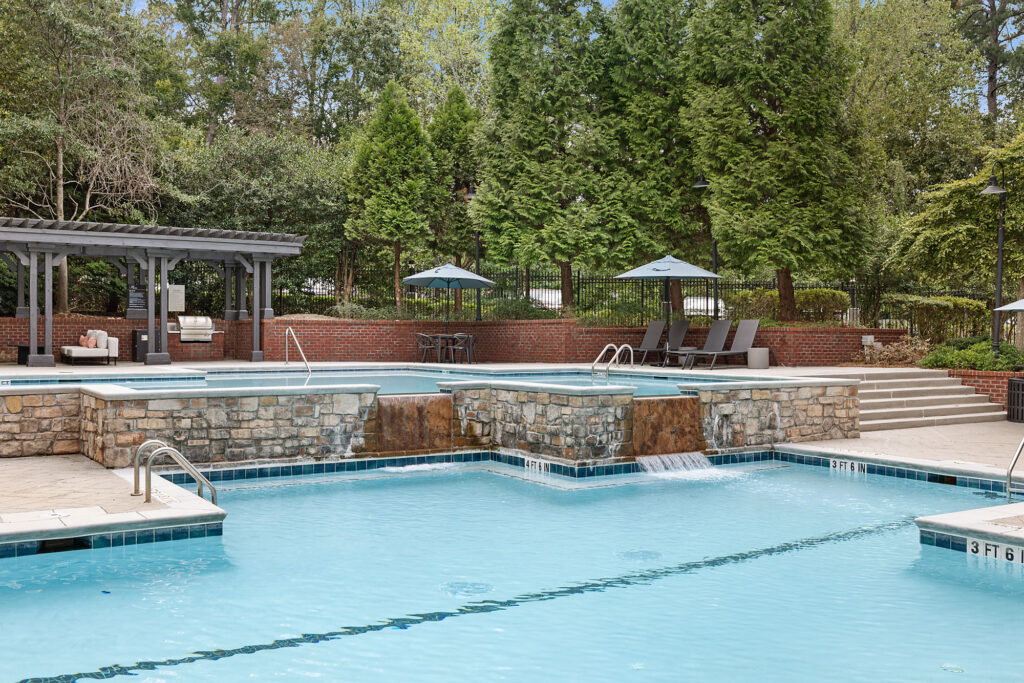 A resort-style swimming pool featuring a stone-faced elevated spa with cascading water, a pergola, and poolside lounge chairs.