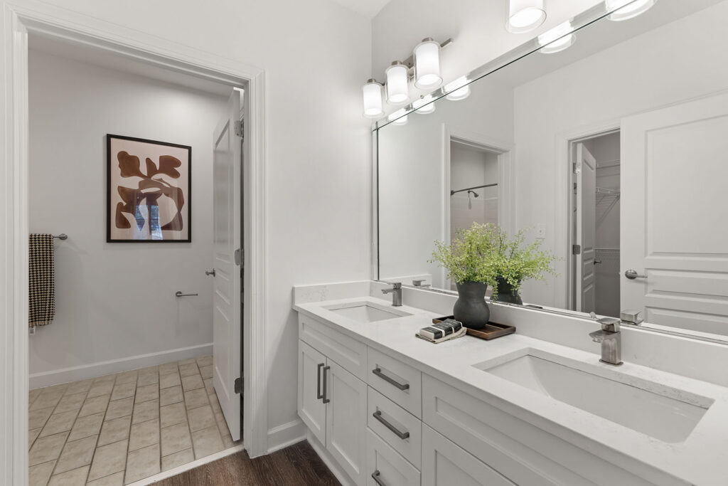 Double vanity bathroom with white cabinets, quartz countertops, and a large mirror reflecting a doorway.
