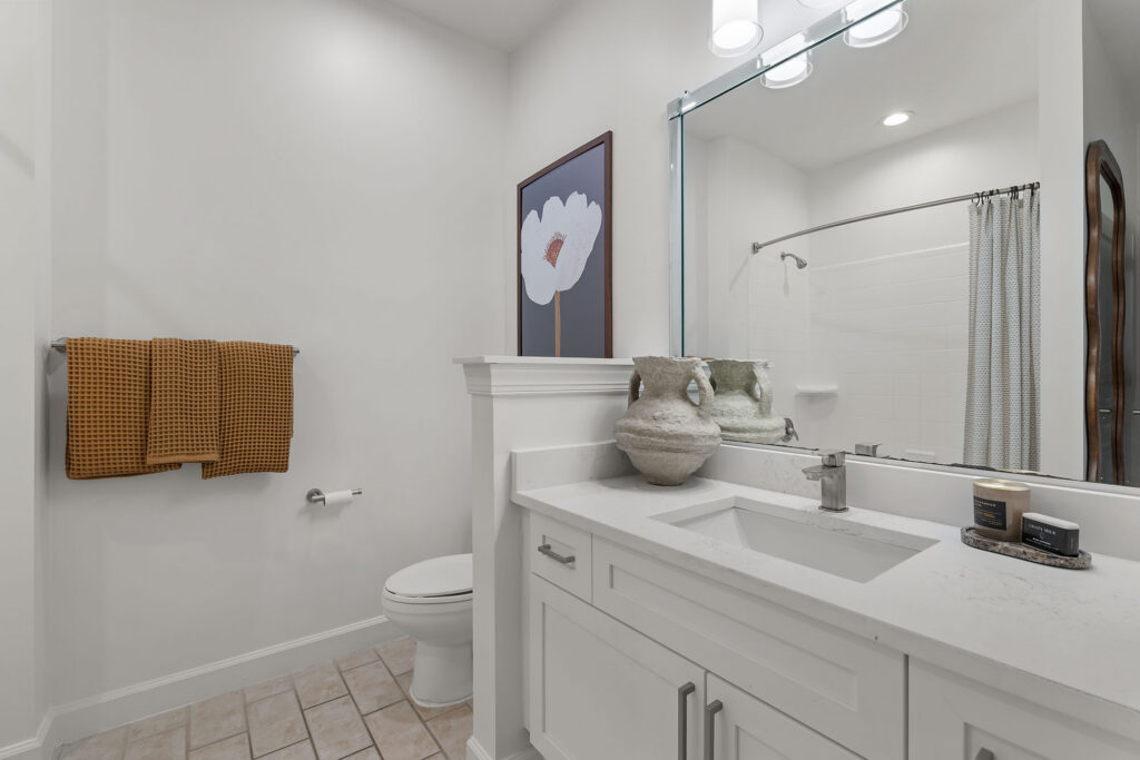 Bathroom with a white vanity, a textured gray vase, a wall-mounted towel rack with mustard-colored towels, and a framed floral print.