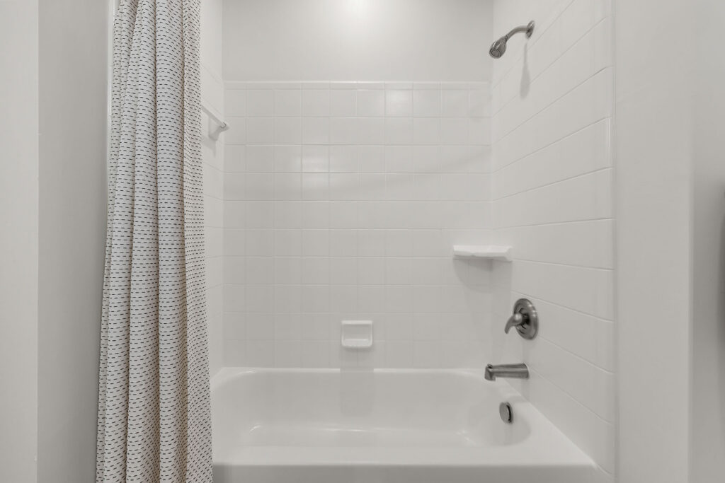 A white bathtub and shower combination with white tile walls, a silver shower head, and a patterned shower curtain.