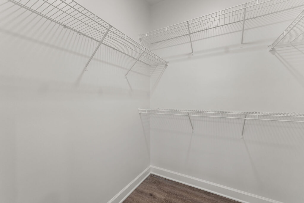 Empty walk-in closet with white walls, wood-look flooring, and white wire shelving mounted in a corner.