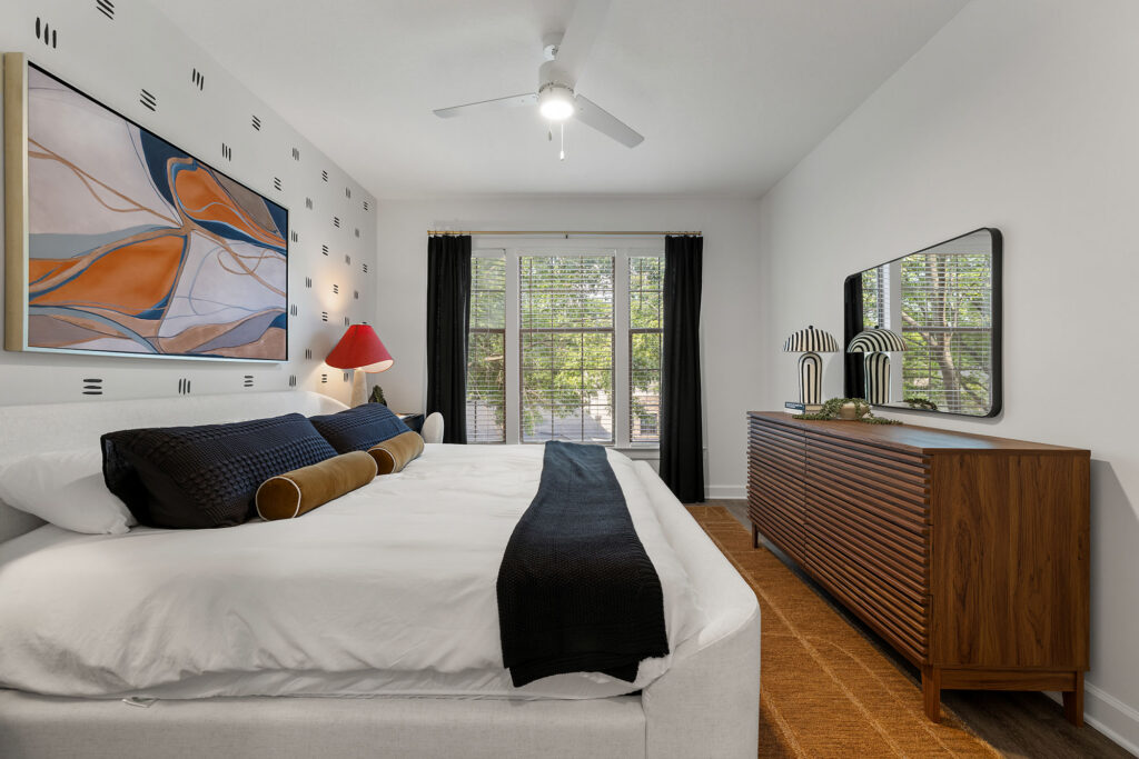 A bedroom with a king-sized bed, a large abstract painting above the headboard, and a wooden dresser with a mirror.