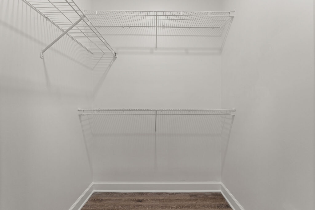 Empty closet with two levels of white wire shelving installed on white walls above wood-look flooring.