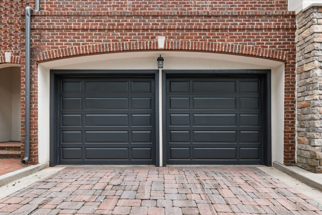 Two dark gray paneled garage doors set within a brick archway above a stone driveway.