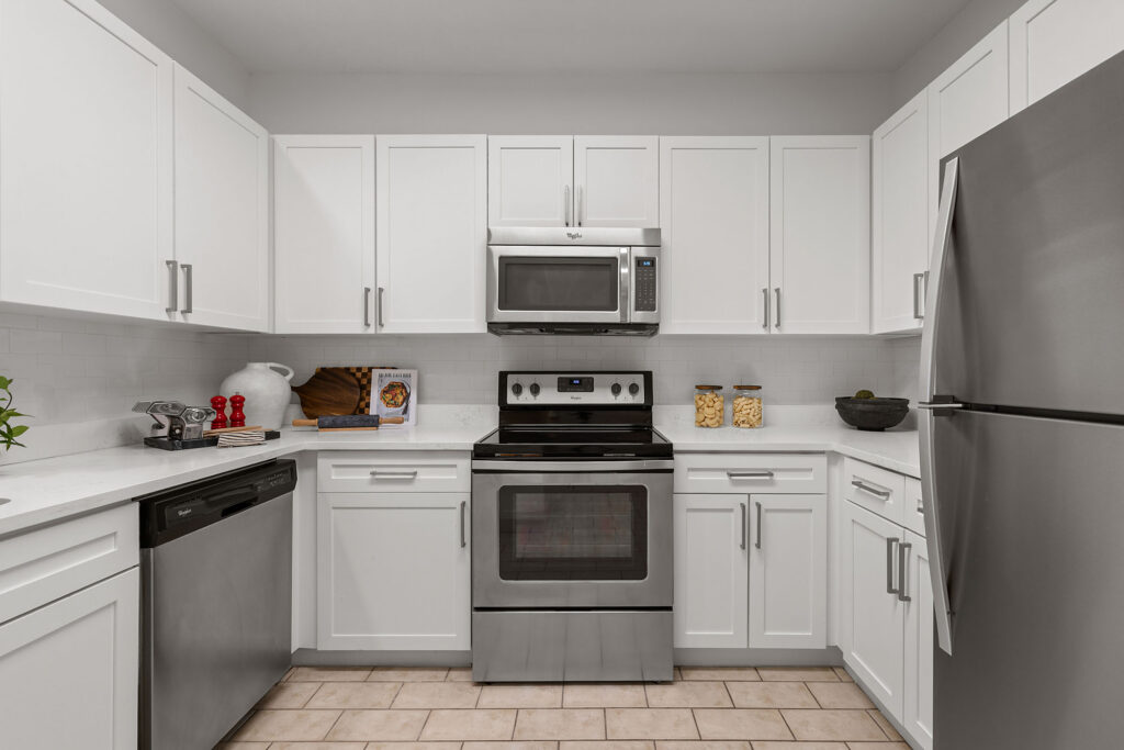 A kitchen with white cabinets, stainless steel appliances, and tiled flooring.