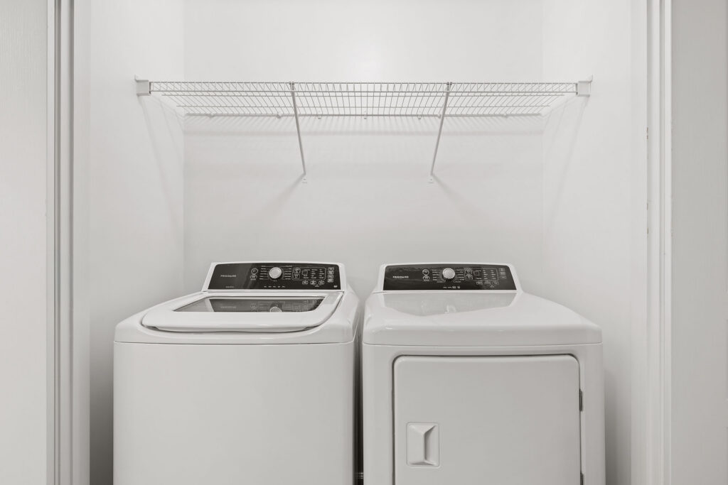 Frigidaire top-load washing machine and dryer inside a laundry closet with a wire shelf above.
