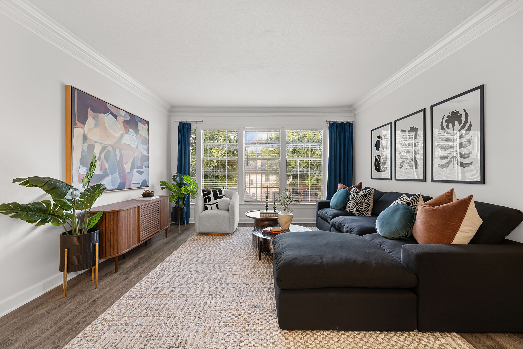 A living room with a large black sectional sofa, a light gray armchair, a wood media console, and a large abstract painting on the wall.